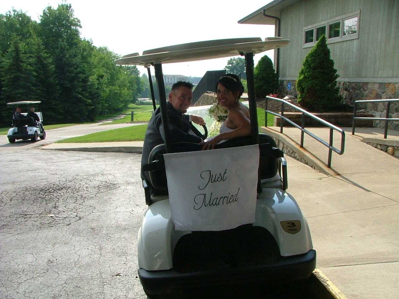 Newlyweds seated in a Just Married golf cart outside their venue