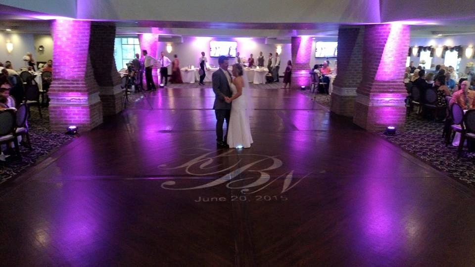Couple dancing on a purple-lit reception floor with a custom monogram